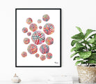 Framed artwork with colorful Herpes Simplex Virus Structure Watercolor on a white wall, next to a plant.