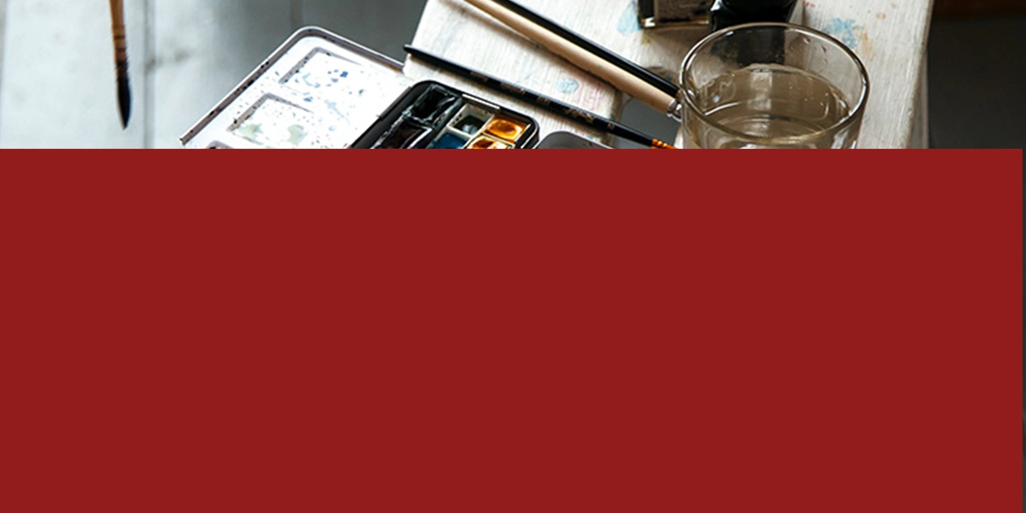 Art supplies, including watercolor paints, brushes, and a glass on a table.